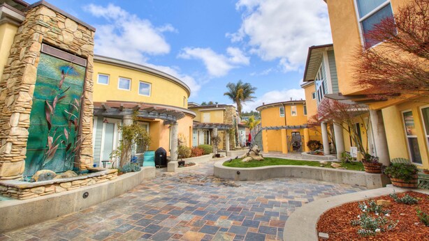 A courtyard with stone walls, a fountain, and a well-maintained lawn. - Fresh look at Shore Pleasure a family fav, steps from beach and downtown (Avila Beach)