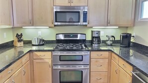 A kitchen with wooden cabinets, a stainless steel stove, a microwave, and a coffee maker. - Fresh look at Shore Pleasure a family fav, steps from beach and downtown (Avila Beach)