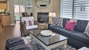 A living room with a fireplace, a sofa, a coffee table, and a dining area with a chandelier. - Fresh look at Shore Pleasure a family fav, steps from beach and downtown (Avila Beach)