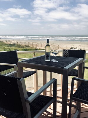 Una mesa con una botella y un vaso en un balcón con vista a la playa.