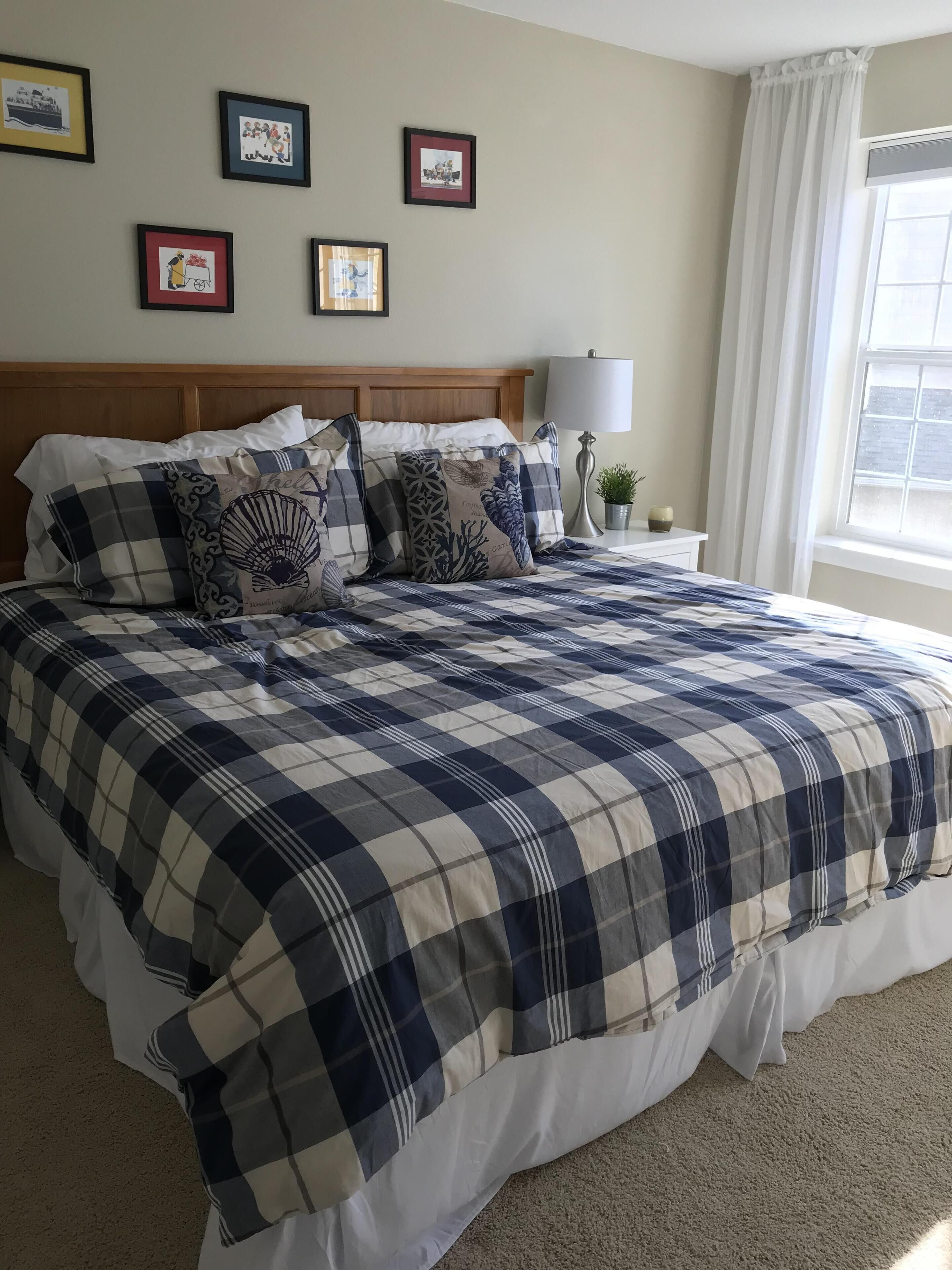A neatly made bed with a blue and white checkered bedspread, a wooden headboard, and four framed pictures on the wall.