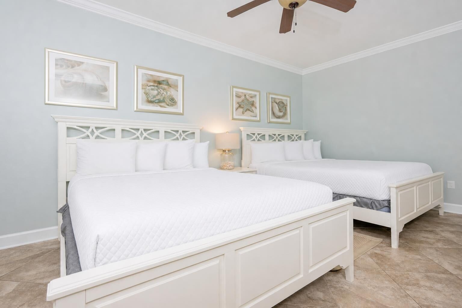 A bedroom with two beds, a ceiling fan, and framed artwork on the wall.