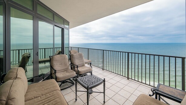 A balcony with two cushioned chairs and a small table, overlooking a body of water. - The Oasis at Orange Beach, formerly known as Phoenix West II, Unit 2402 (Orange Beach)