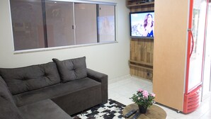 Ein Wohnzimmer mit einer Couch, einem Fernseher, einem Kühlschrank und einem kleinen Tisch mit einer Blumenvase.