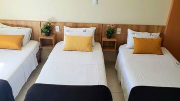 Três camas de solteiro com roupa de cama branca e almofadas amarelas, cabeceiras de madeira e pequenas mesas de cabeceira com plantas em vasos.