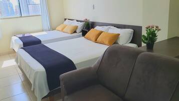 Habitación de hotel con dos camas, un sofá, una mesita y una planta en maceta.