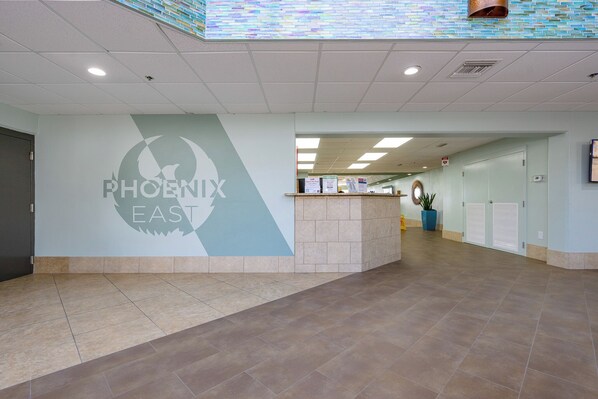 Un hall d’entrée spacieux avec un comptoir de réception, un logo fixé au mur et un sol carrelé.