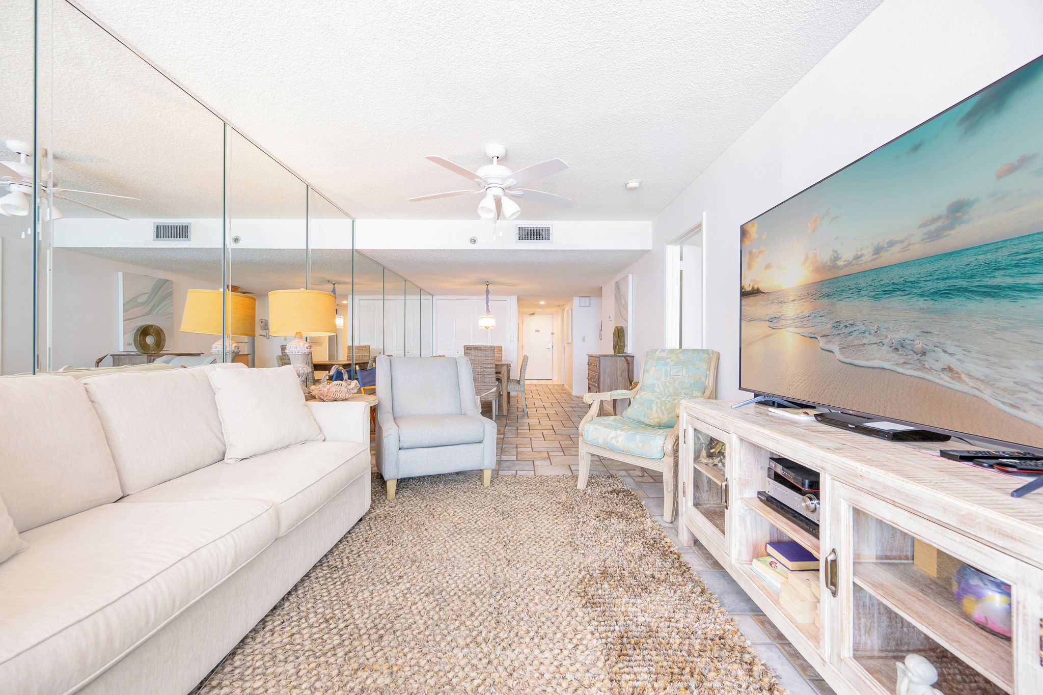 A modern living room with a white sofa, a television, and a large painting of a beach scene.
