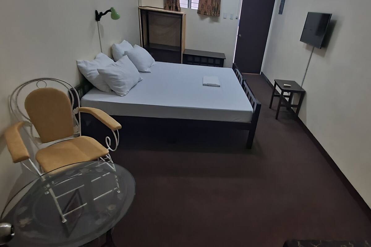 Una habitación con cama, silla de ruedas, una mesita y televisor.