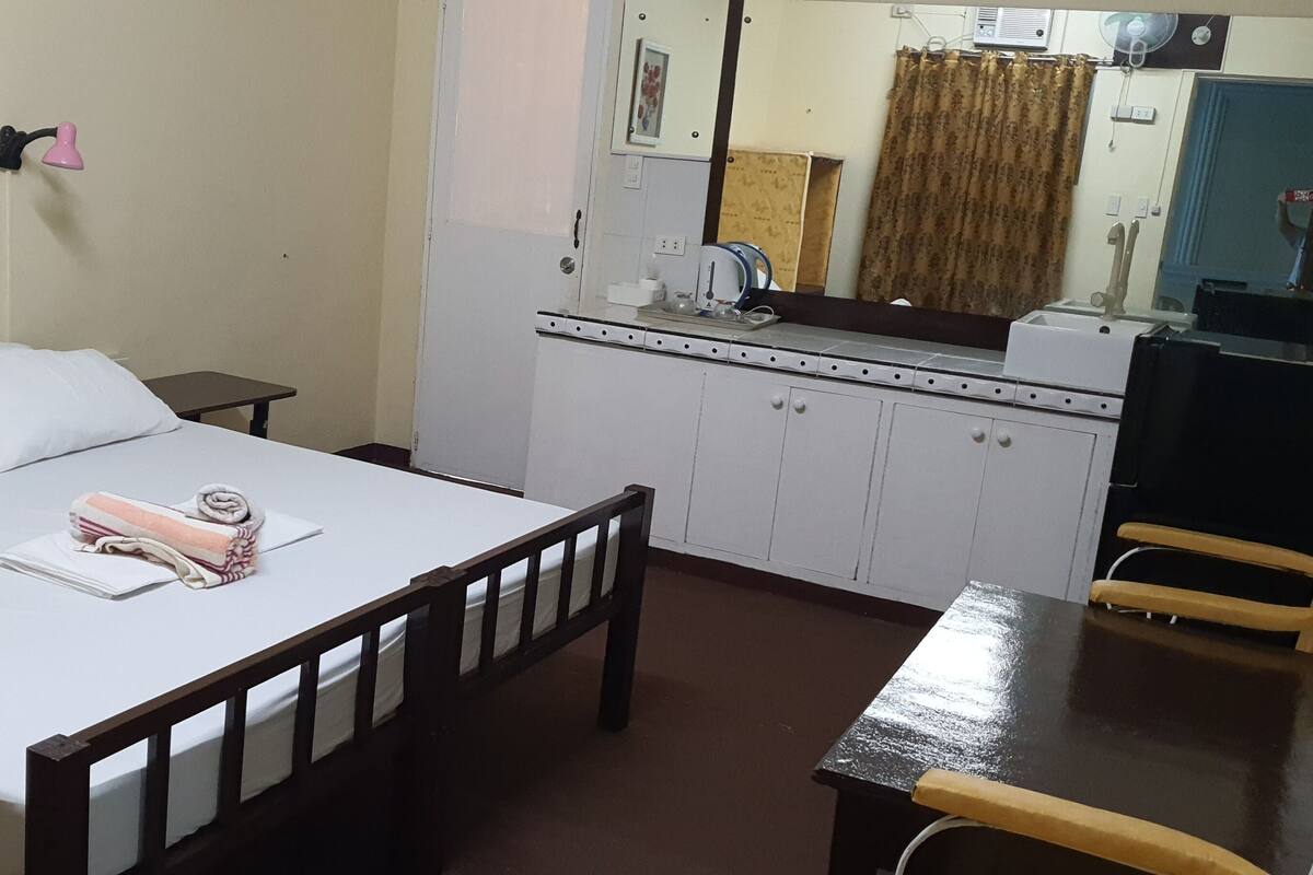 Un dormitorio con cama, una mesita, una silla, un espejo, un lavabo y un televisor.