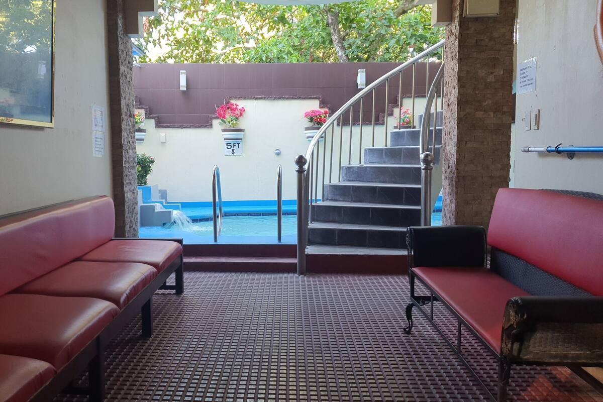 Un área de recepción con una escalera que lleva a una piscina, bancos y suelo de baldosas.
