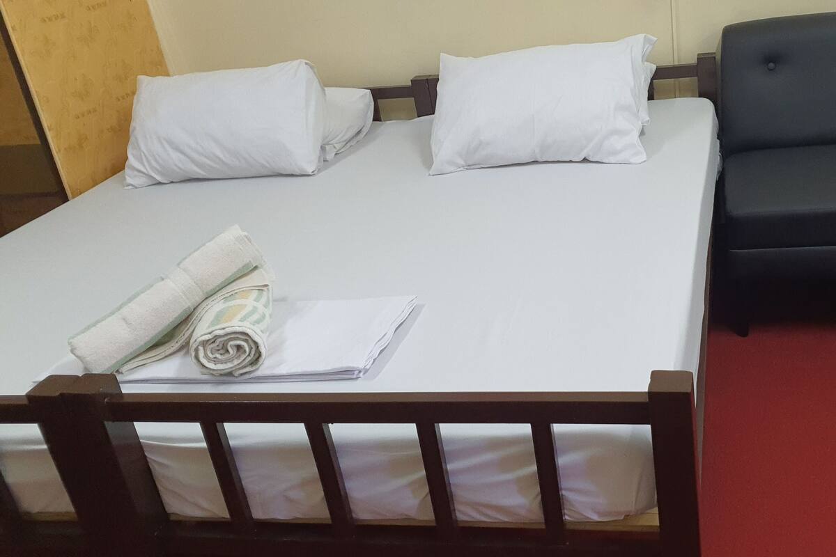 Una cama bien hecha con sábanas y almohadas blancas, un sofá negro y un cabecero de madera.