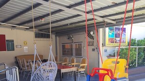 A covered outdoor seating area with a swing chair, a dining table with chairs, and a yellow and blue play structure. - Cool Martin Resort Hotel (Bacoor City)