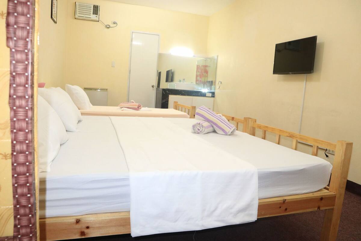Una cama individual con estructura de madera, un televisor de pantalla plana montado en la pared y un espejo sobre la cama.