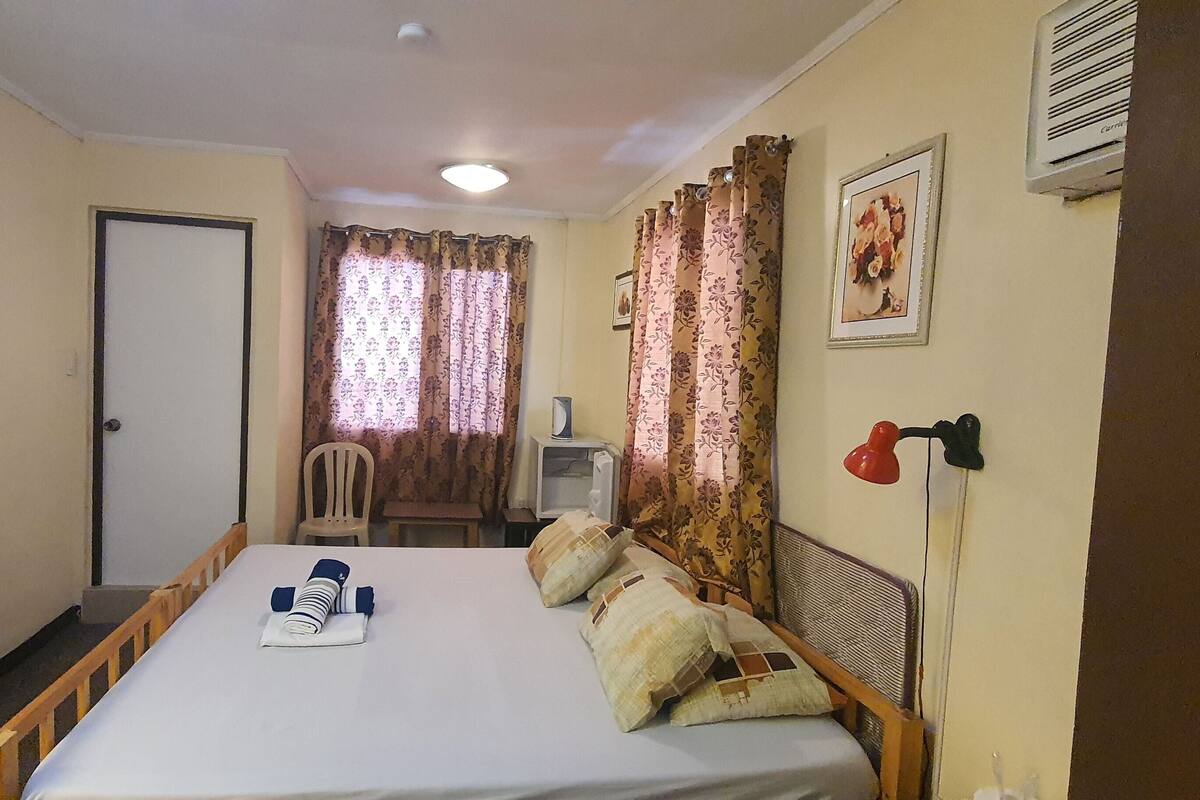 Habitación de hotel con cama, televisión montada en la pared, escritorio con silla y ventana con cortinas.