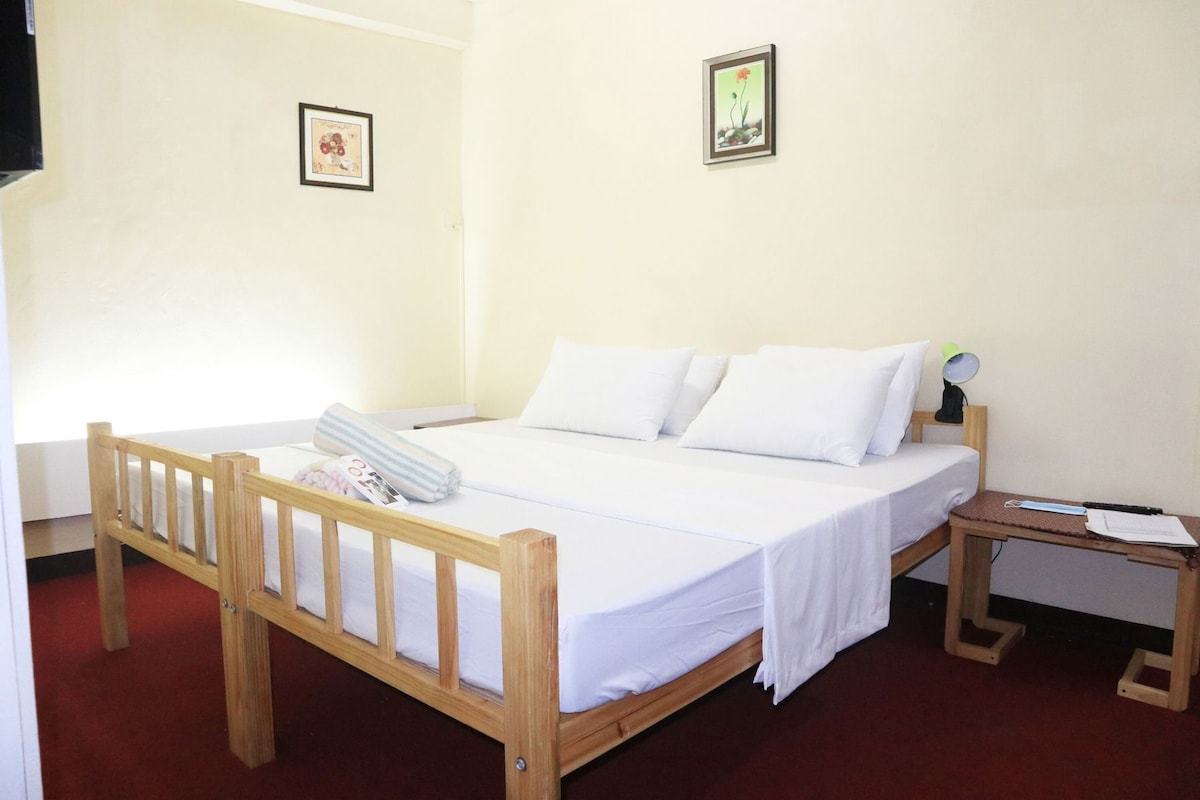 Una cama individual con estructura de madera, ropa de cama blanca y una mesita de noche pequeña con una lámpara.
