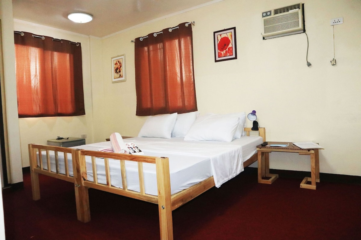 Una cama individual con estructura de madera, una mesita de noche, una lámpara y un aire acondicionado instalado en la pared.