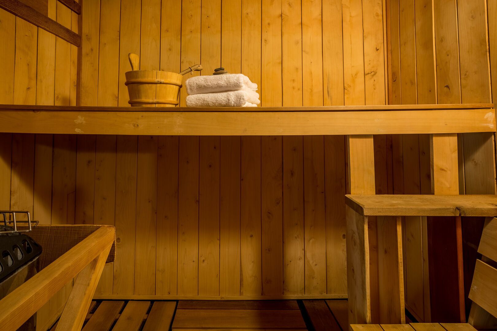 Un sauna en bois avec des bancs, un seau en bois et des serviettes sur une étagère.