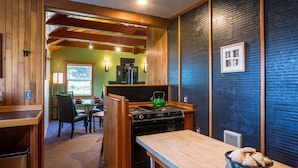 A compact kitchen with a stove, a green kettle, and a dining area with a table and chairs. - Zen Beach Retreat-Relaxing Sauna - Steps to a Sandy Beach! (Yachats)