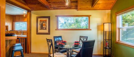 A dining area with a round table, four chairs, and a window with a view of greenery.