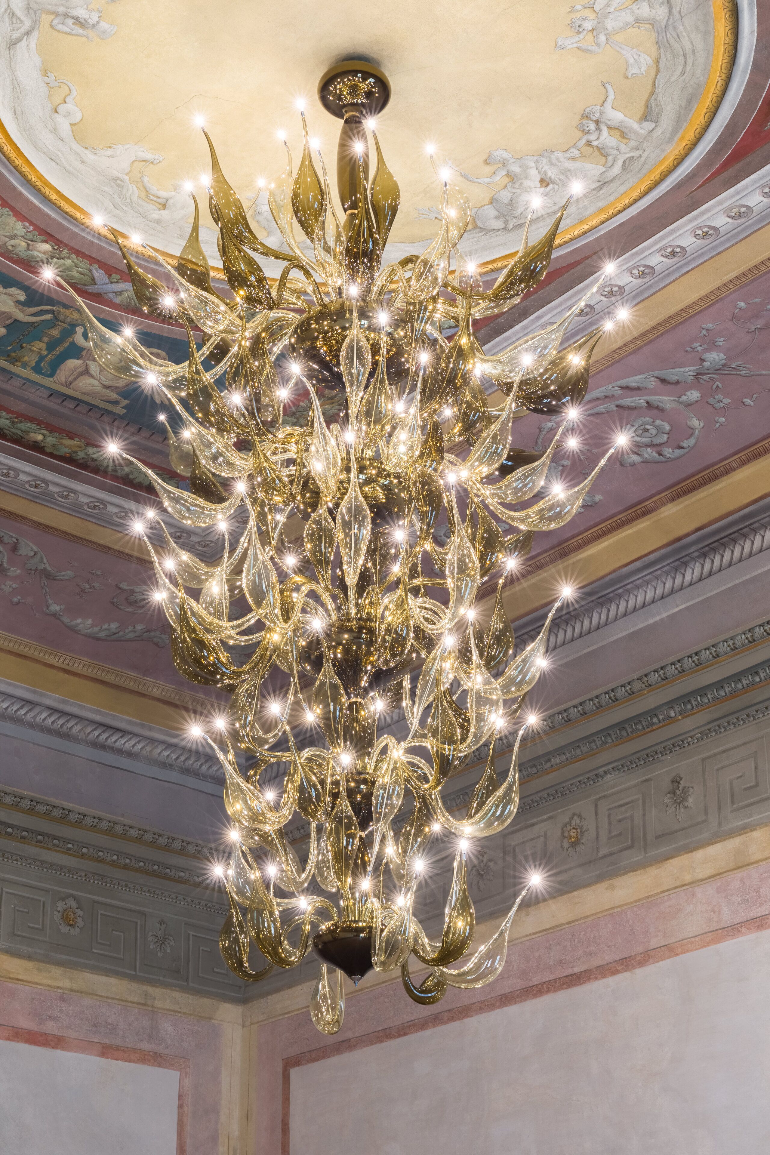 Un candelabro con múltiples fuentes de luz en una habitación con decoración ornamental en el techo.