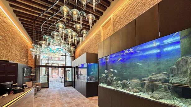 A lobby with a large aquarium, a chandelier, and a reception area. - Hotel Aquarius Venice (Venice)
