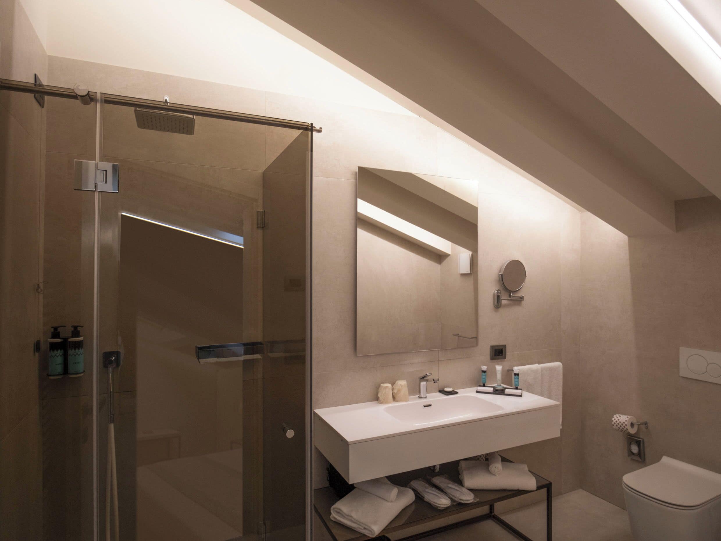 A modern bathroom with a glass shower enclosure, a white sink with a mirror above, and a toilet to the right.