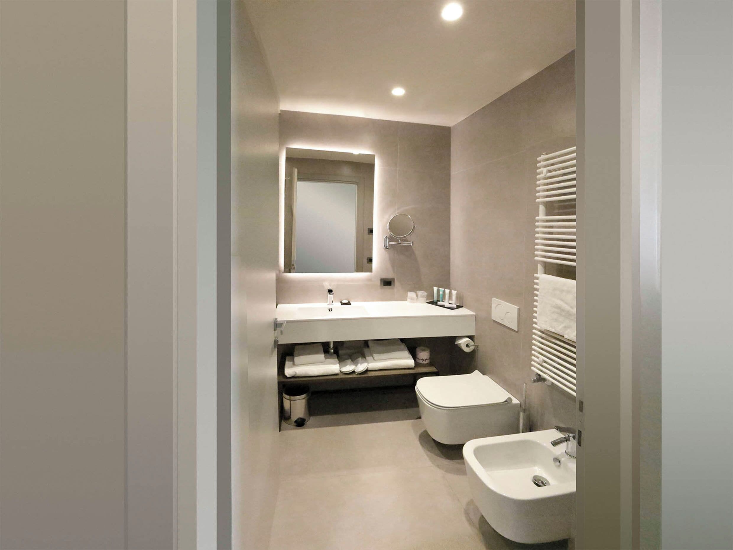 A modern bathroom with a white sink, two bidets, a mirror, and a towel rack.
