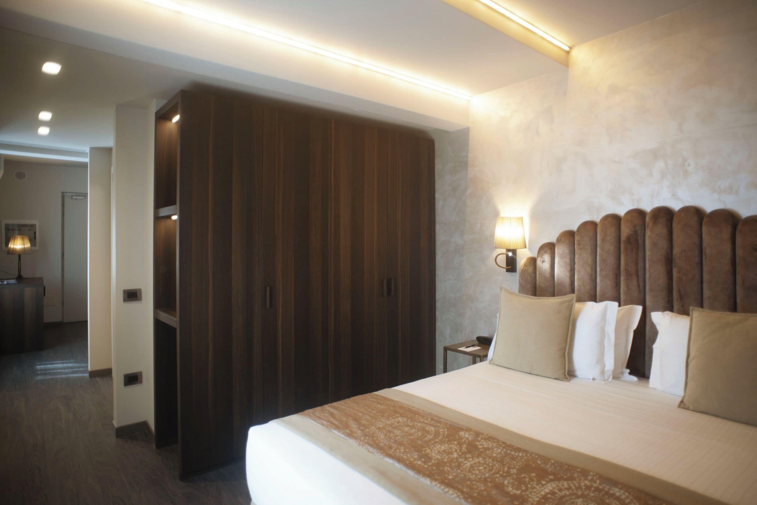 Een hotelkamer met een groot bed, een kledingkast, een nachtkastje en een wandlamp.
