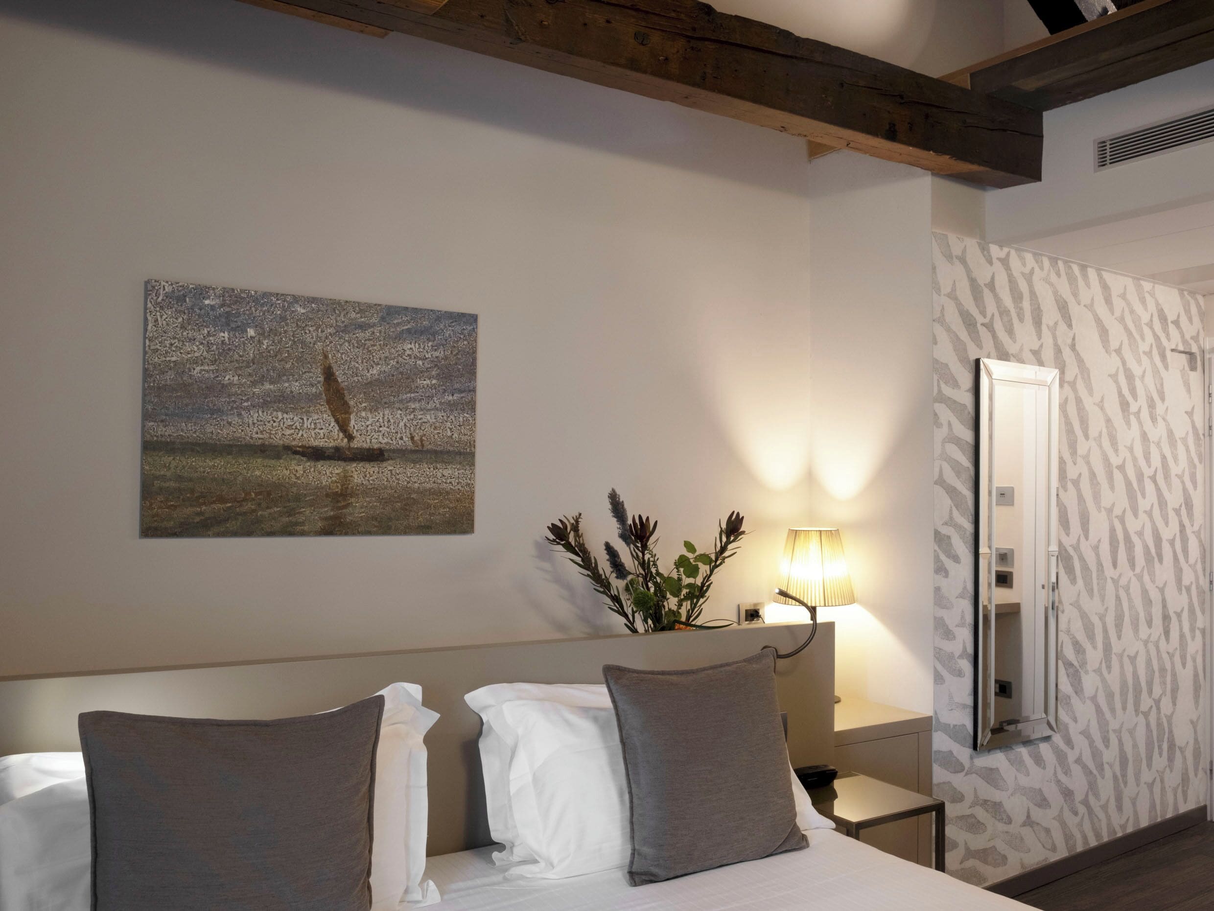 Une chambre d’hôtel comprenant un lit, une table de chevet, une lampe, un miroir et un mur orné d’un motif texturé.