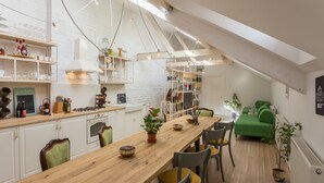 Une cuisine moderne avec une table à manger en bois, des meubles blancs et une chambre à l’étage avec un canapé vert.
