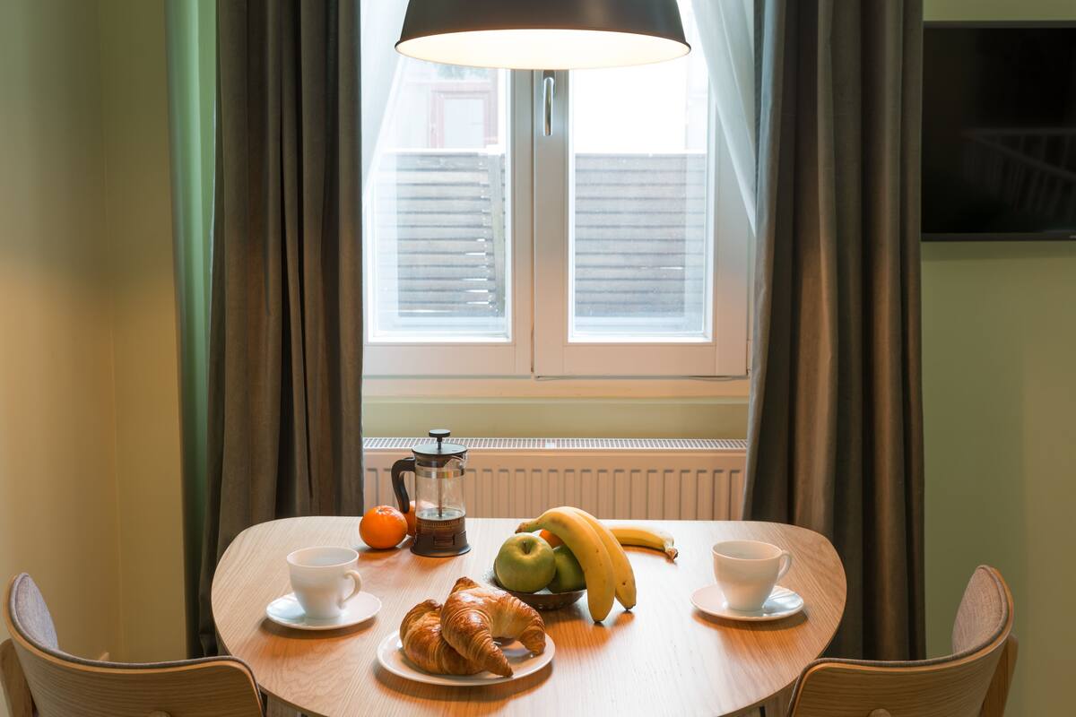 A breakfast table with croissants, bananas, apples, and a coffee pot.