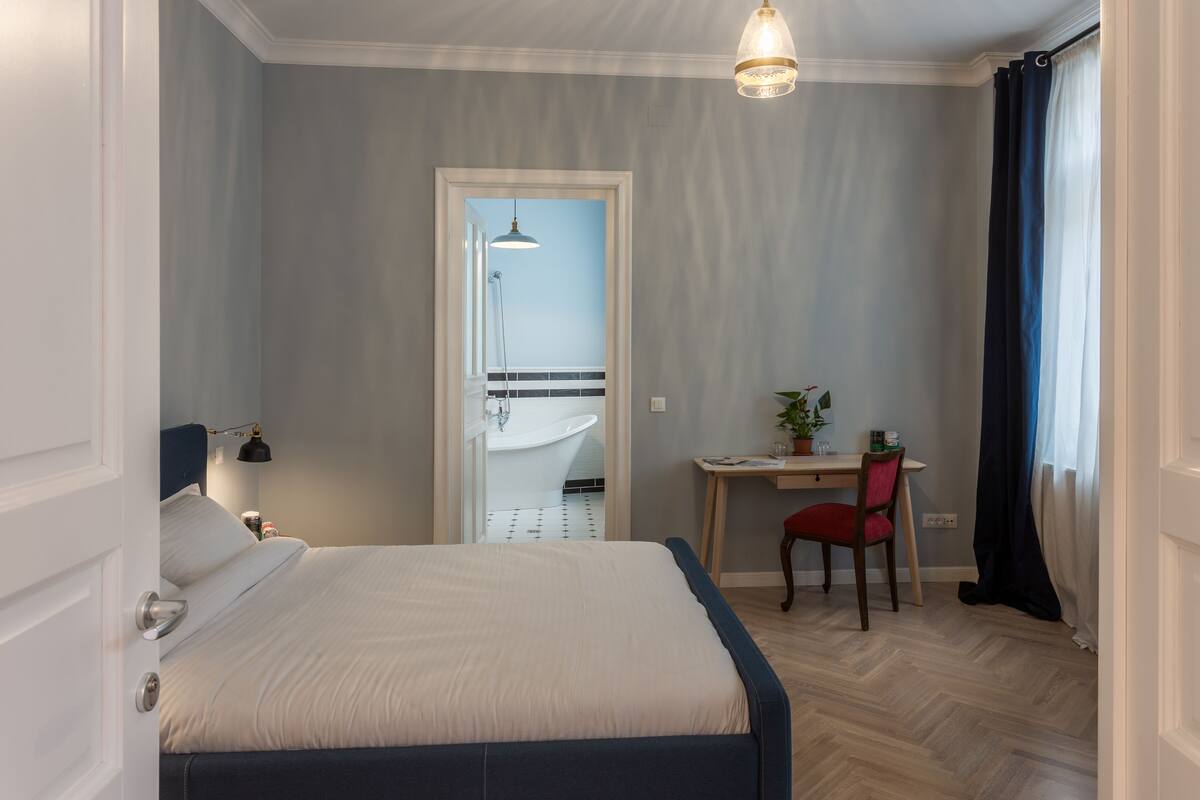 A bedroom with a bed, desk, chair, and a bathroom visible through an open door.