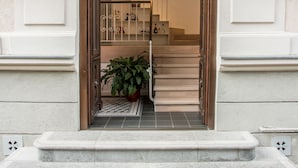 Une entrée imposante avec un escalier menant à l’étage supérieur, un pot de fleurs à sa base et des luminaires fixés au mur.
