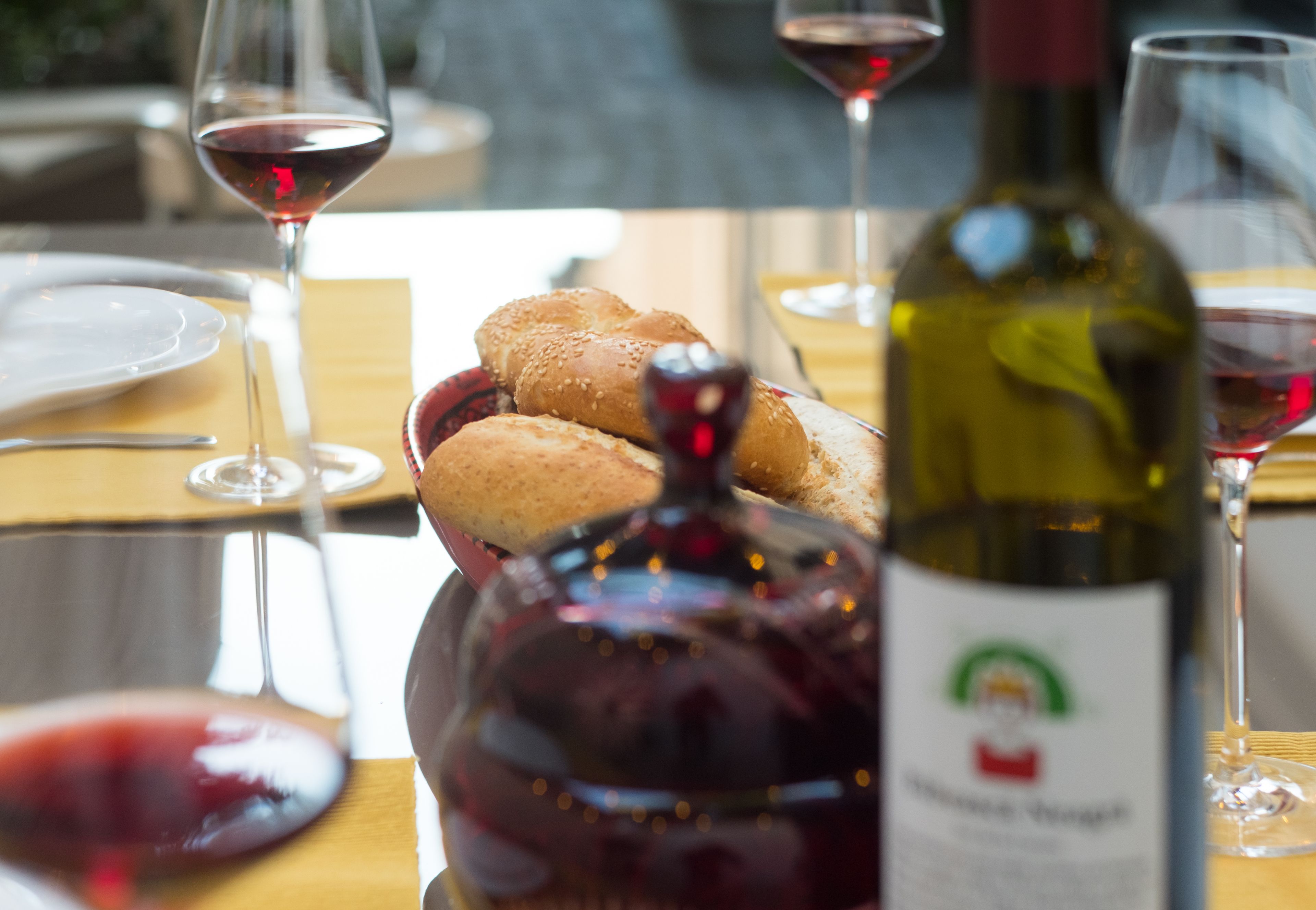 Una mesa de comedor con una botella de vino, copas y una cesta de pan.