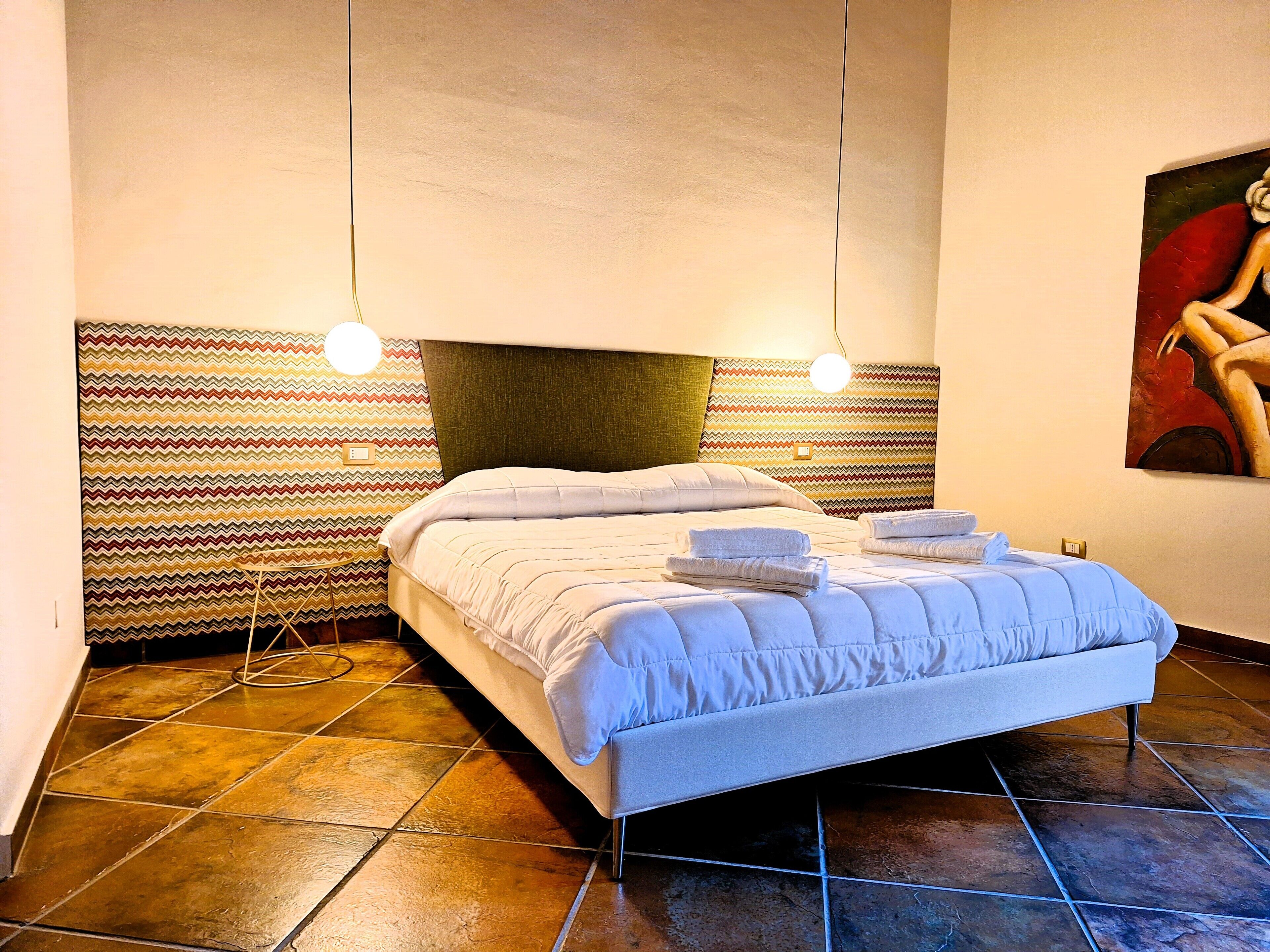 A bed with a white duvet and two pillows, a patterned wall, and a painting on the wall.