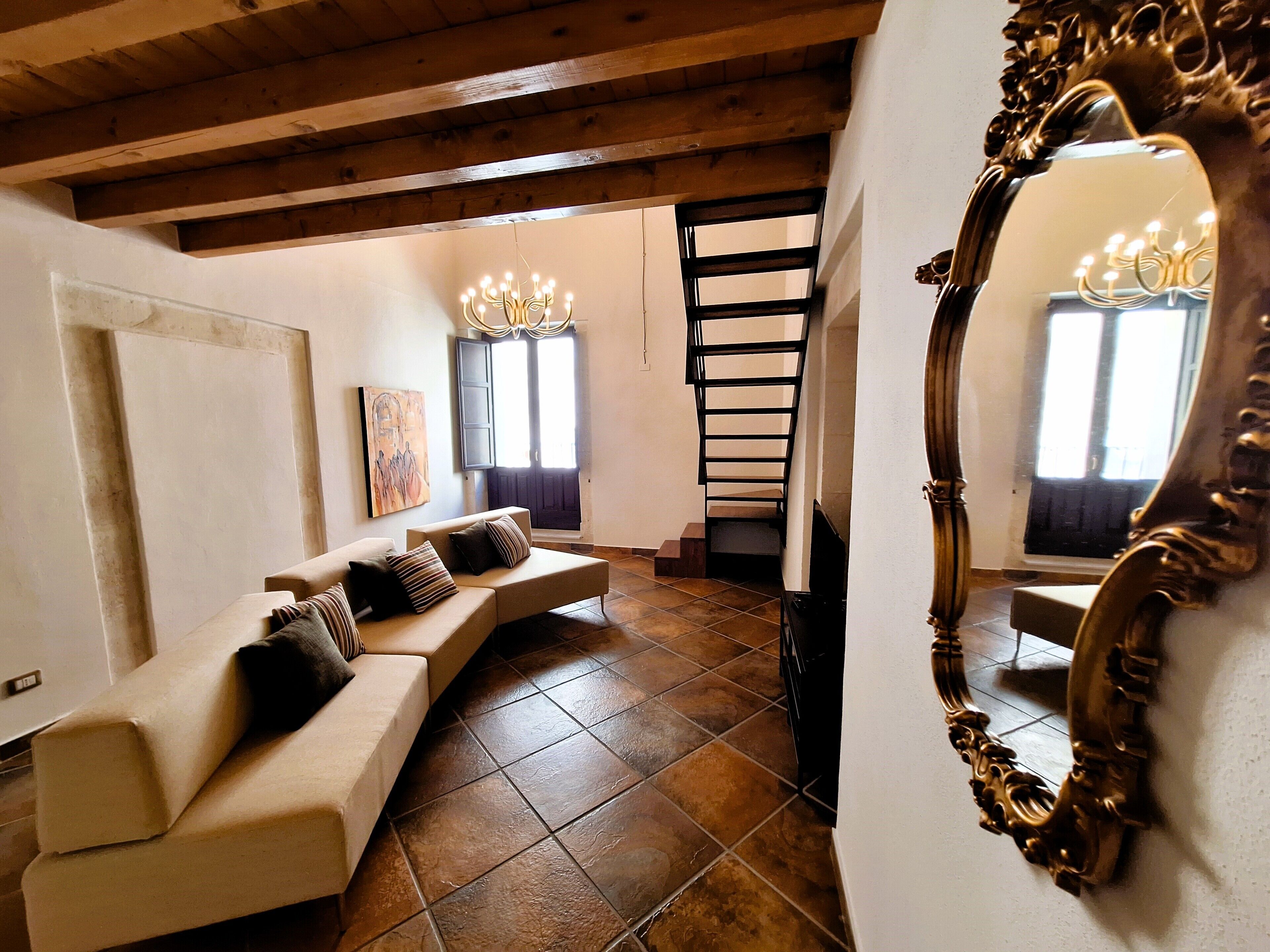 A living room with a sofa, a staircase, a chandelier, and a large mirror.