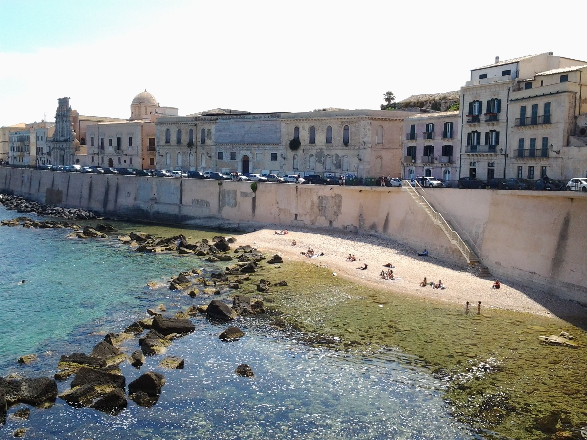 Una zona costera con un litoral rocoso, una playa arenosa y una hilera de edificios con una torre y cúpula destacadas.