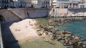 A coastal area with a sandy beach, clear water, and rocky outcrops. - Casa Aretusa (Syracuse)