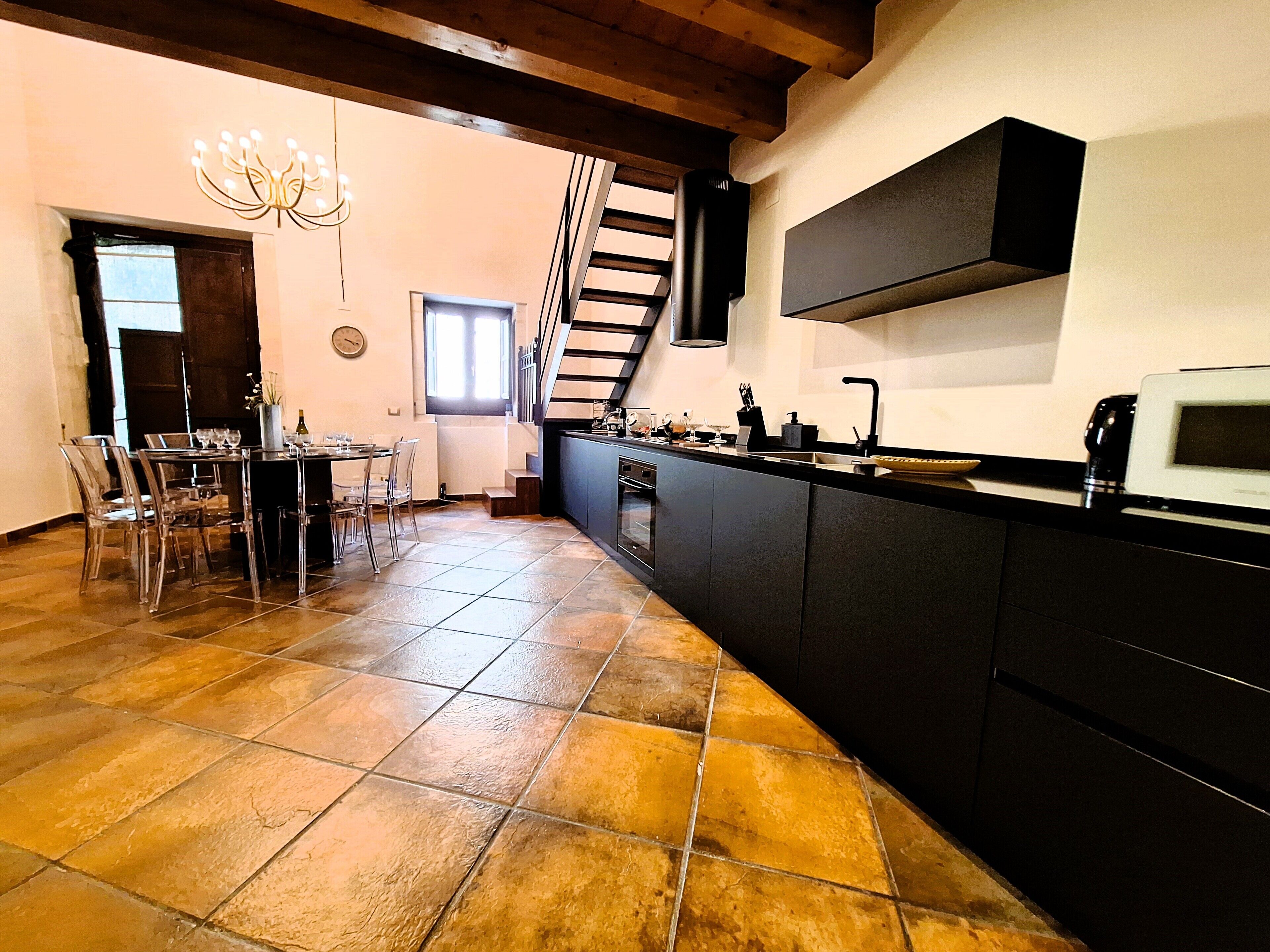 Une cuisine dotée d’un plan de travail noir, d’un four encastré et d’un four à micro-ondes. On y trouve également un coin repas avec une table et des chaises.