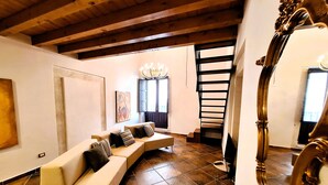 A modern living room with a curved sofa, a chandelier, and a staircase leading to an upper level. - Casa Aretusa (Syracuse)