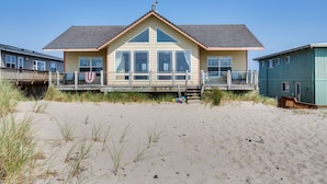 Een huis aan het strand met een groot terras, meerdere ramen en een overdekte veranda.