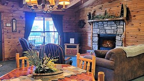 A cozy log cabin interior with a stone fireplace, wooden furniture, and a large window with curtains. - Lake Shore Cabins on the Waterfront of Beaver Lake with Boat Dock & Swim Deck (Eureka Springs,)