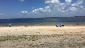 Une plage avec un ciel dégagé et une eau calme. On y trouve plusieurs parasols et chaises de plage.