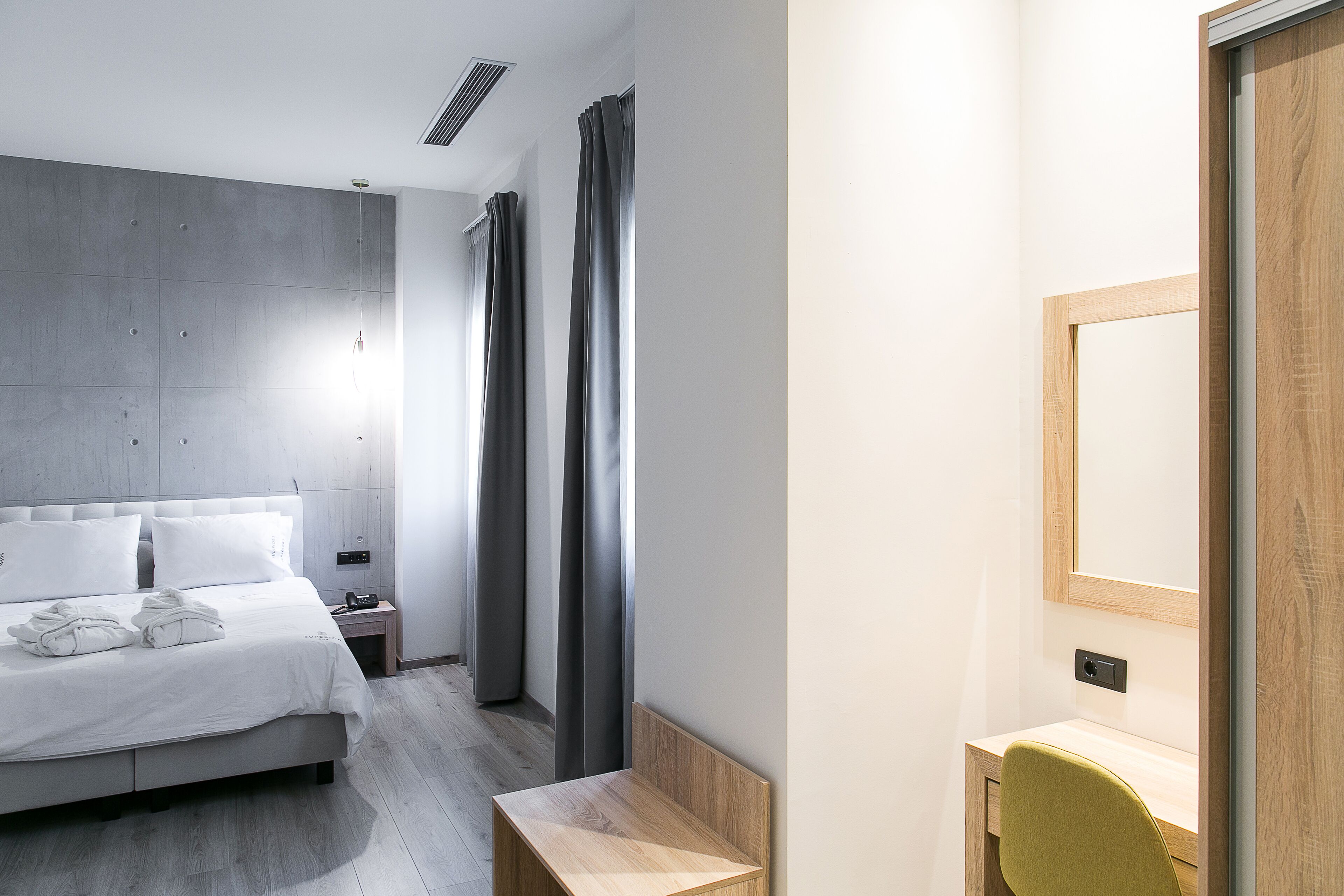 A modern hotel room with a large bed, a bedside table, a desk, and a mirror.