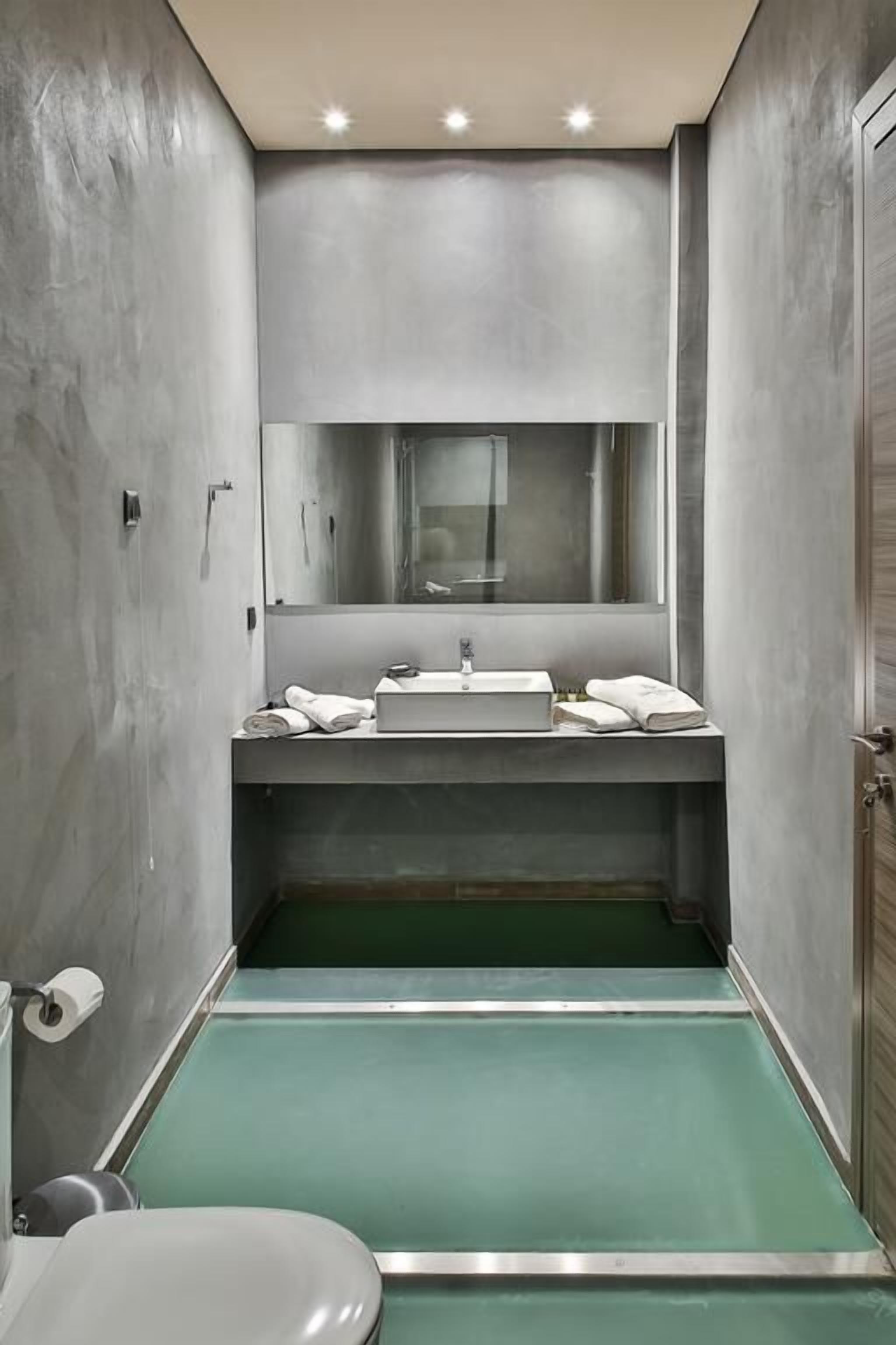 A narrow bathroom with a green floor, a white sink, and a mirror above it.