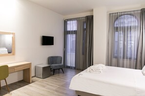 Une chambre d’hôtel équipée d’un lit, d’un bureau, d’une chaise, d’une télévision et de grandes fenêtres avec des rideaux.
