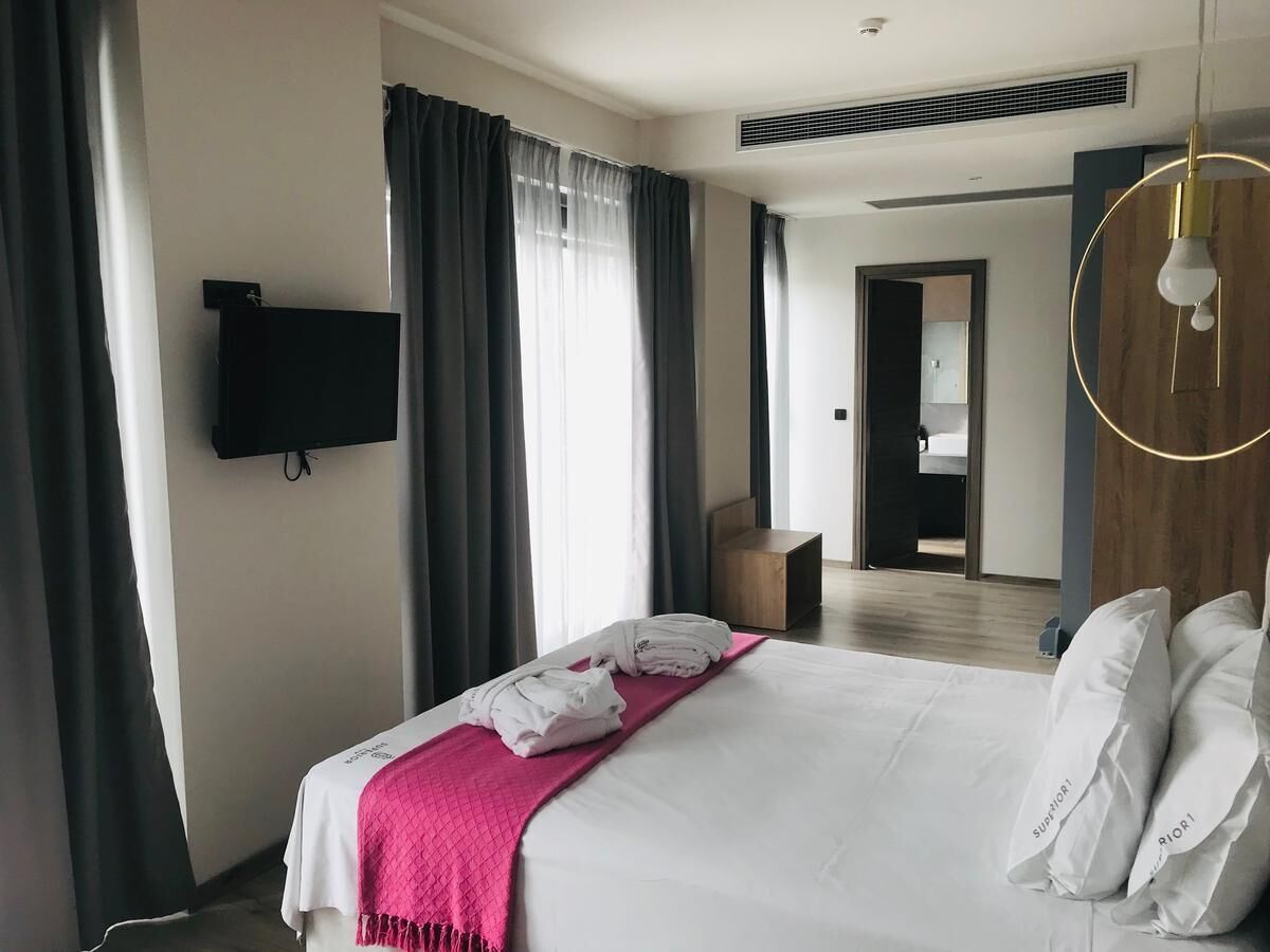 A modern hotel room with a large bed, a flat-screen TV mounted on the wall, and a wooden headboard.