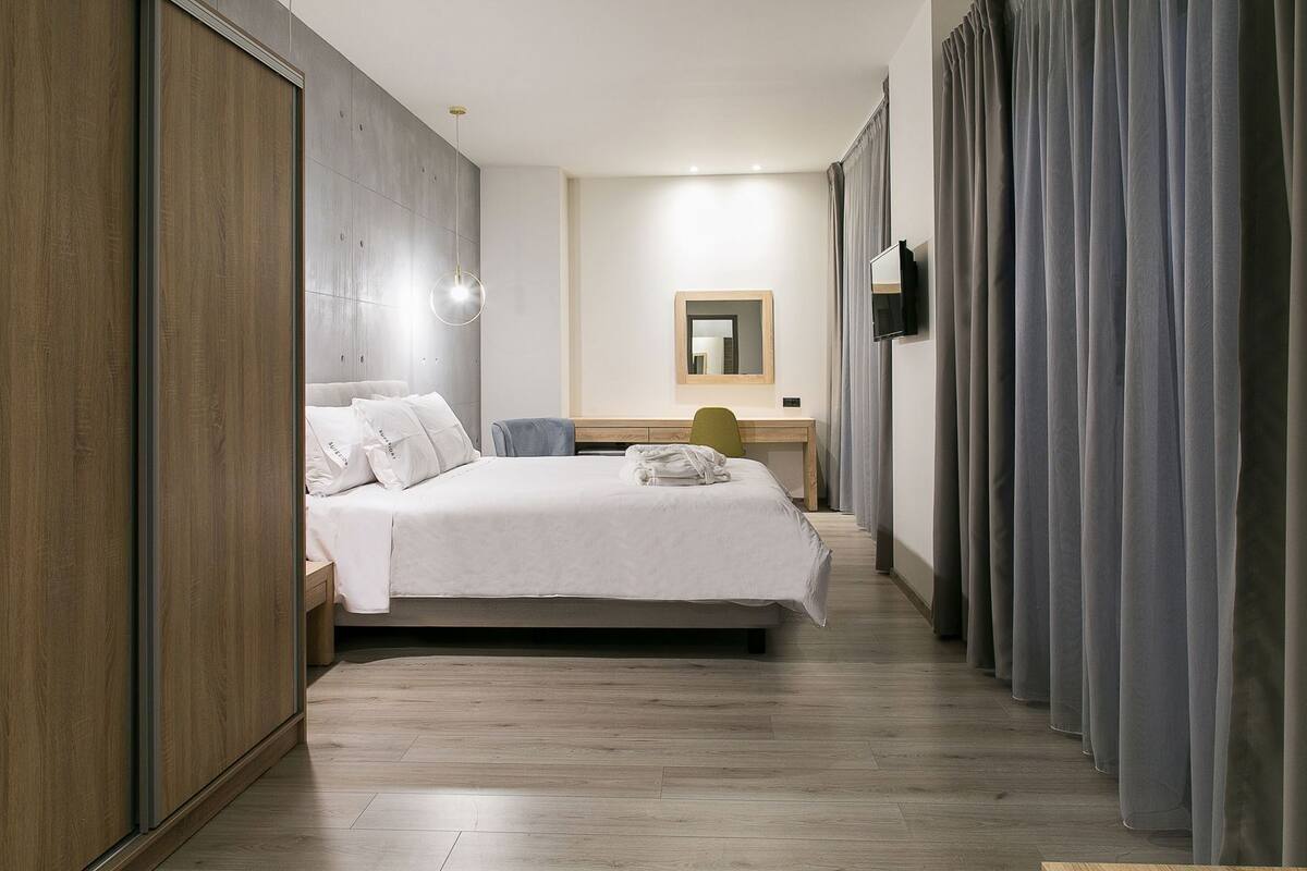 Une chambre d’hôtel avec un lit, un bureau, une chaise, un miroir et des rideaux.