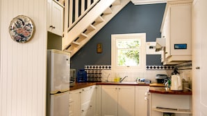 Une cuisine avec des meubles blancs, un réfrigérateur, une fenêtre et un escalier.